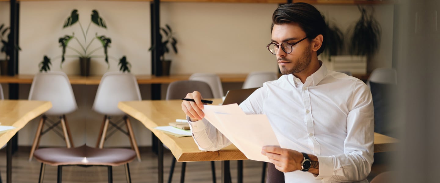 Jovem empresário sério em óculos trabalhando pensativamente com papéis no escritório moderno
