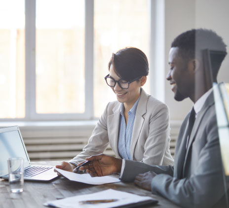 Um dos jovens corretores apontando para documento financeiro enquanto discutem os dados com seu colega no escritório