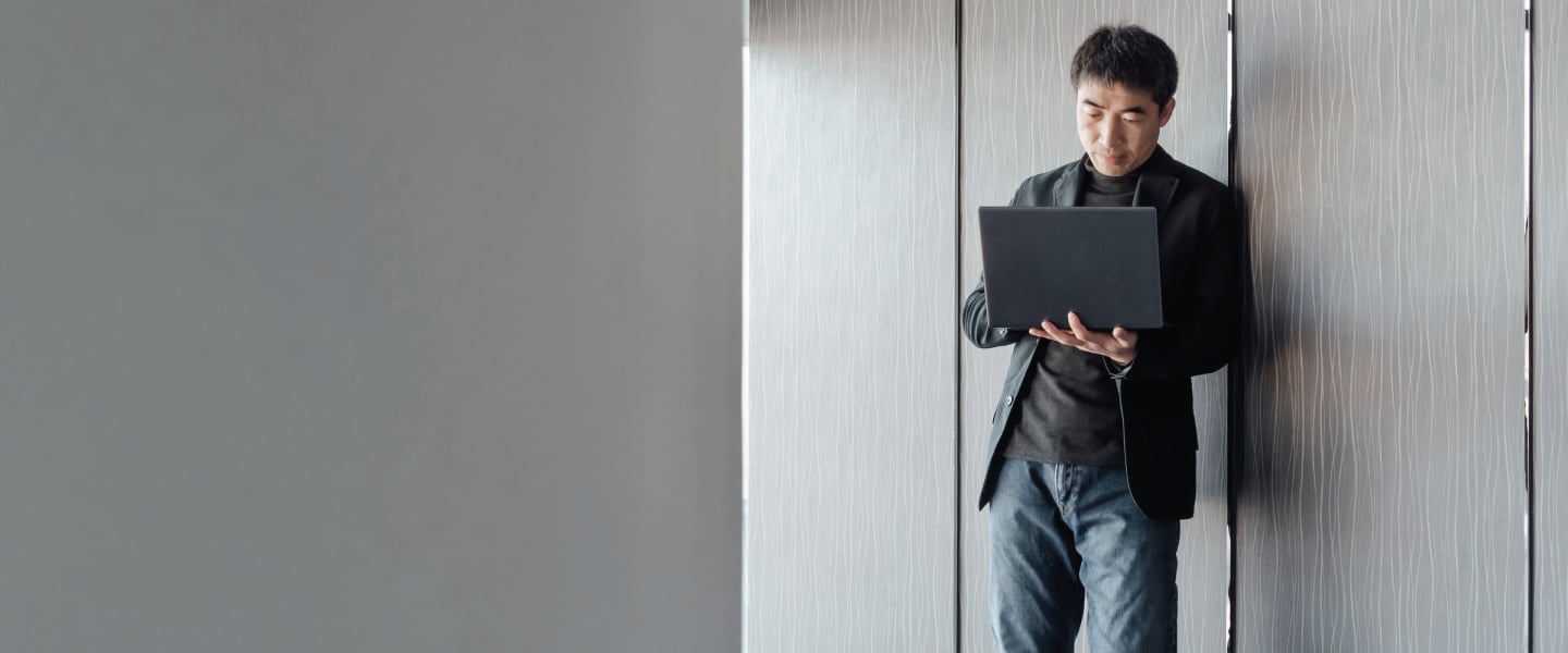Homem asiático encostado na parede com computador na mão