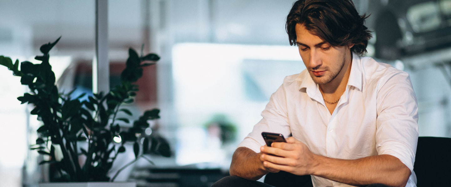 Homem branco mexendo no celular em sala branca
